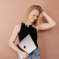 blonďatá žena stojící před hnědou zdí držící notebook